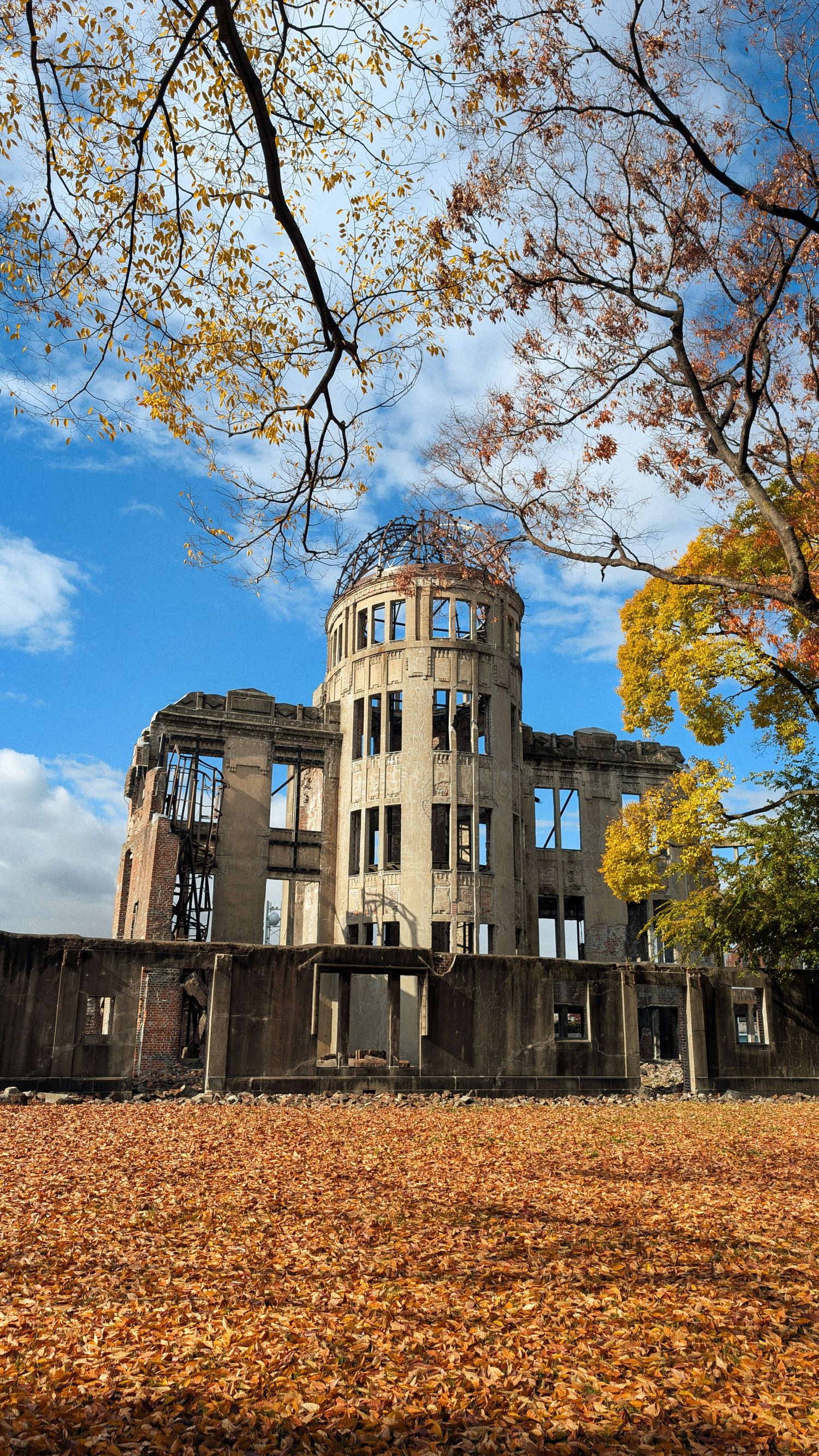 Hiroshima Peace Memorial Atomic Bomb Dome framed by autumn trees and a ground covered in golden fallen leaves.