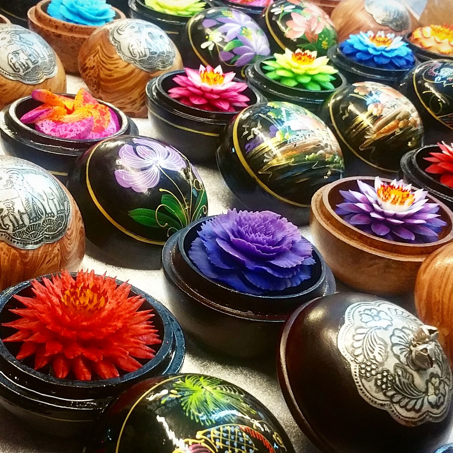 Colorful carved flower lacquer boxes in red, purple, blue and green displayed on a table at a Thai handicraft market.