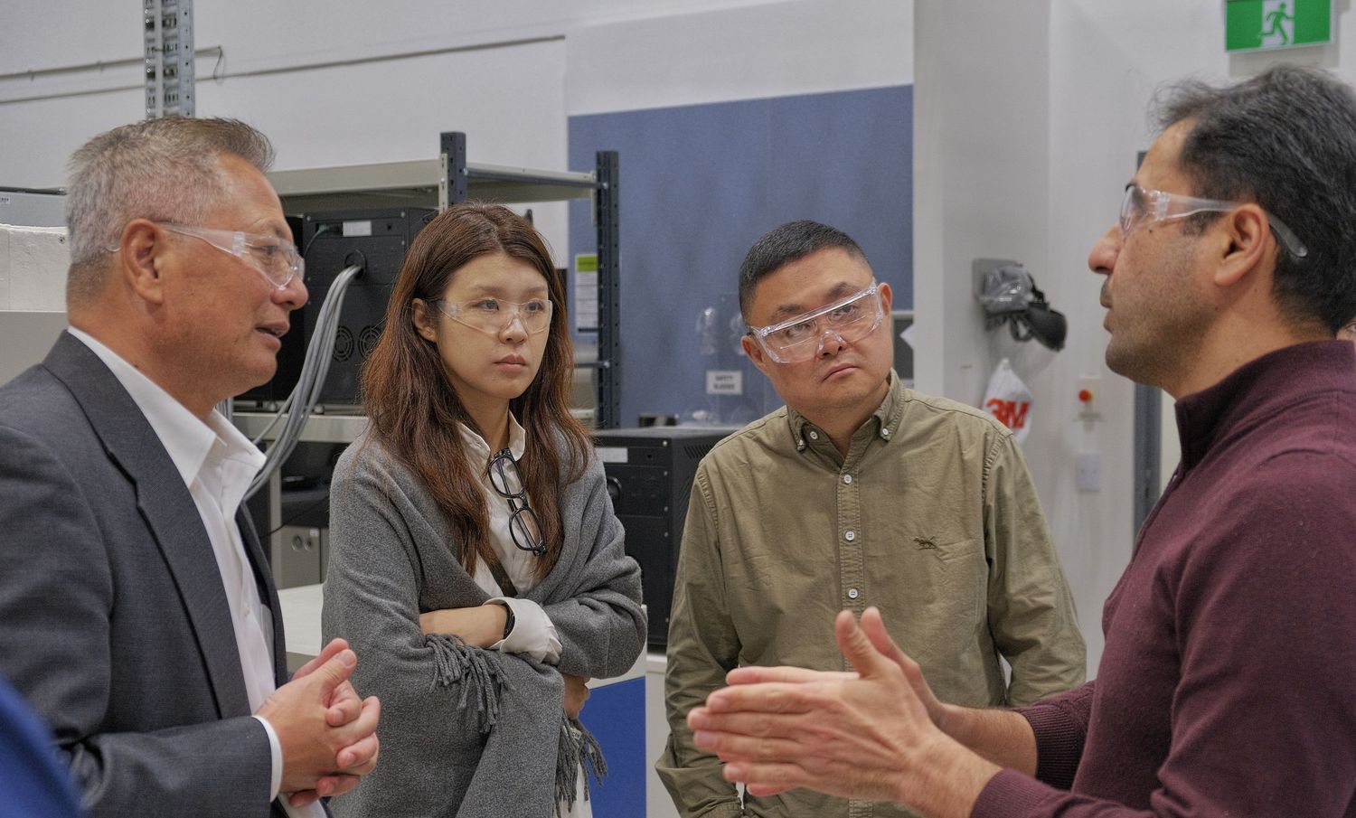 Four people gather in a laboratory discussing research, with a man in a maroon sweater gesturing in the foreground.