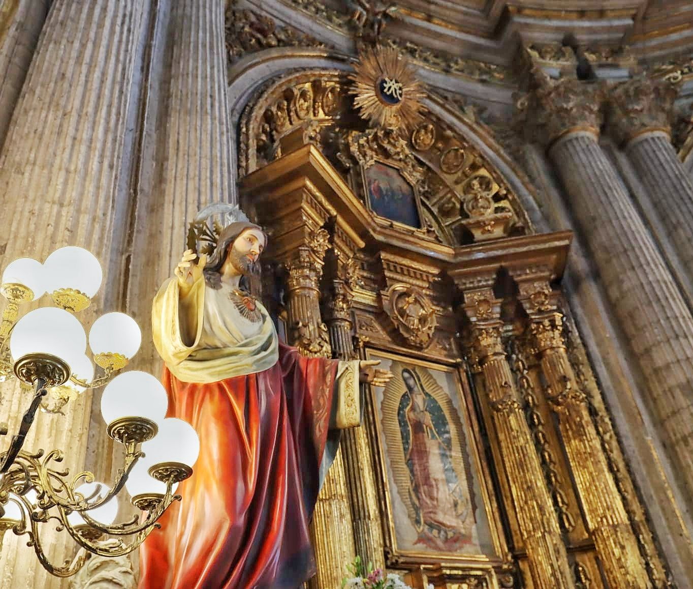 Painted statue of Jesus beside a gilded baroque altar with a Virgin of Guadalupe image, stone columns and a globe chandelier.