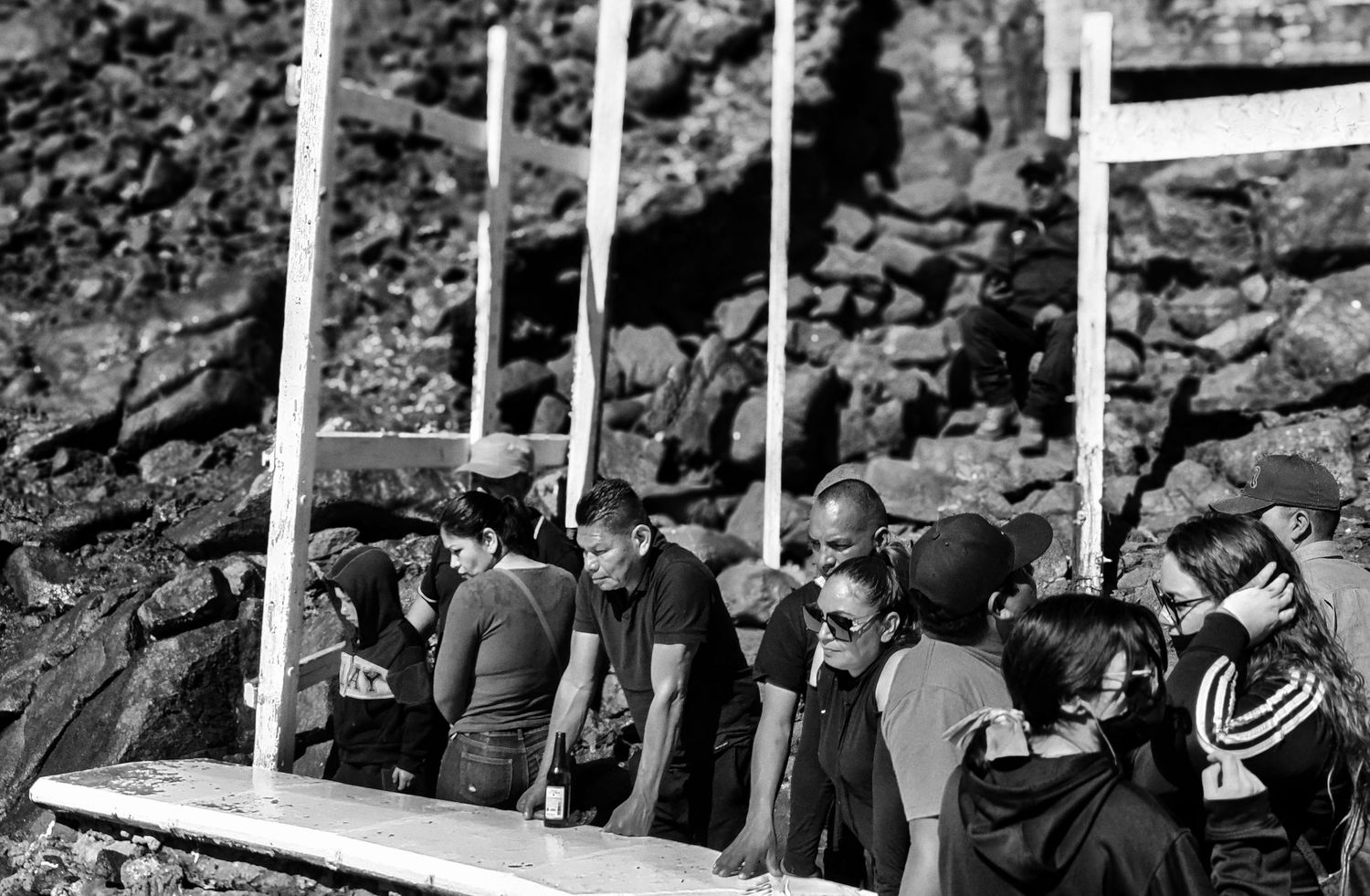 Black and white photo of a crowd gathered beside a rocky hillside, watching intently from behind white railings.