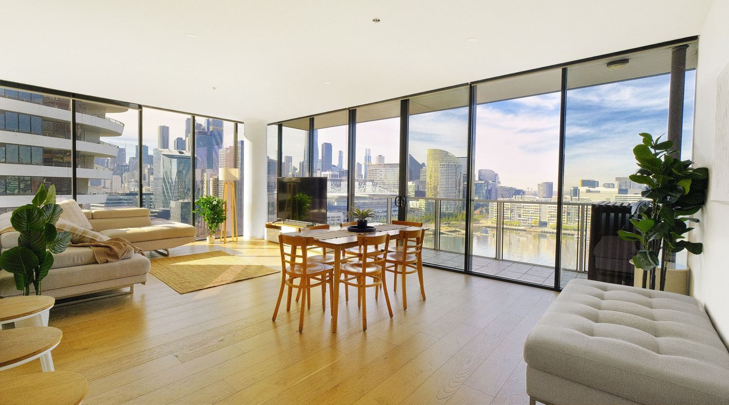 Bright open-plan living and dining area with timber floors, floor-to-ceiling windows and sweeping city views.