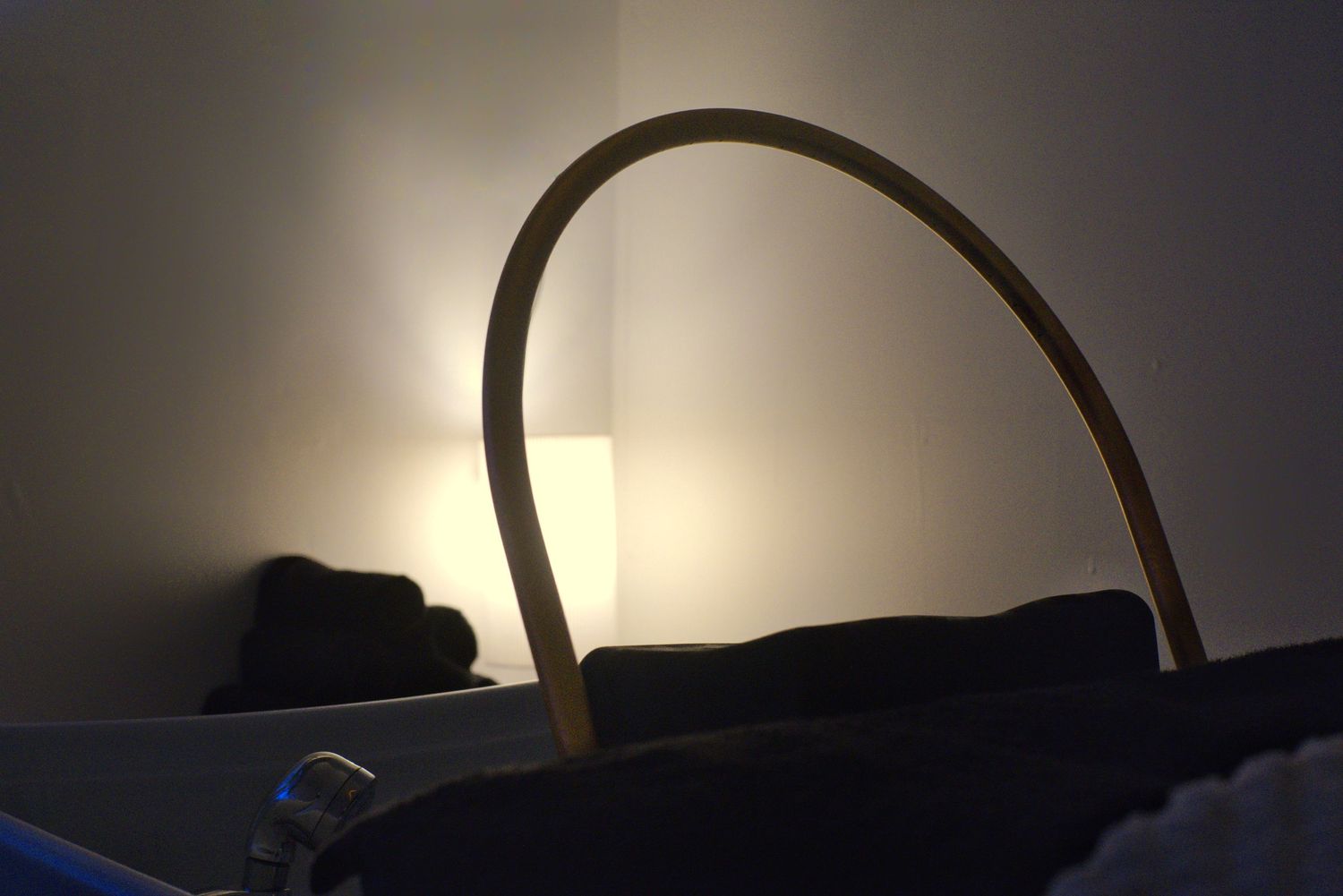 Silhouette of a curved arch beside a massage bed with softly glowing lamplight and rolled towels in a dimly lit spa room.