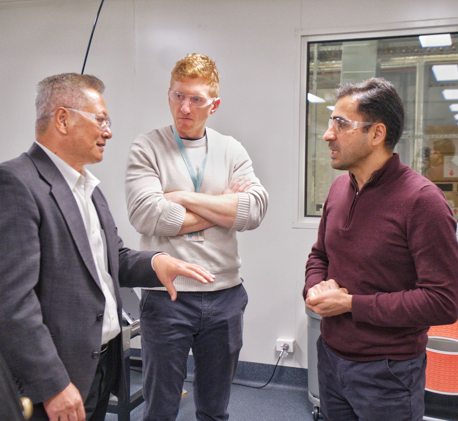 Three men in conversation inside a research facility, one gesturing as he speaks to two colleagues.