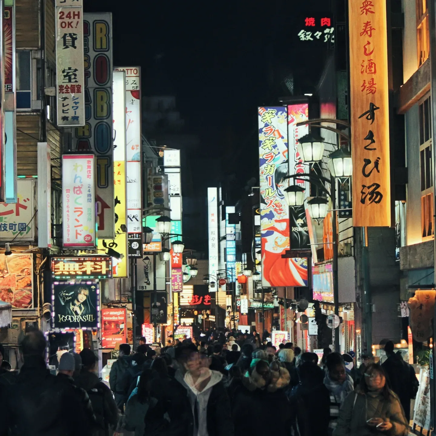 Crowded nighttime street in Japan glowing with colorful neon signs and vertical Japanese-language banners above busy pedestrians.