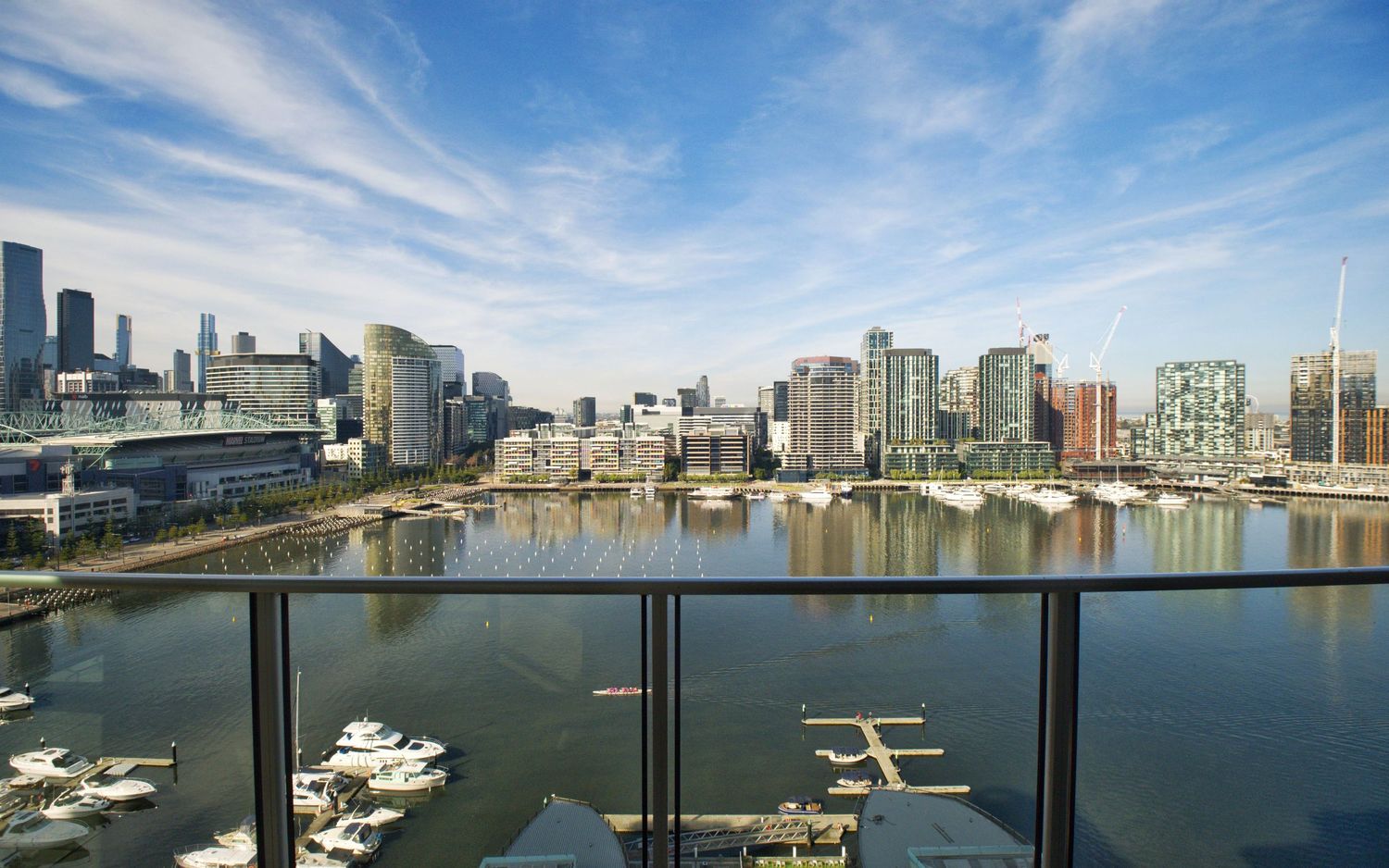 Balcony glass balustrade overlooking a marina with moored boats and a waterfront city skyline under blue sky.