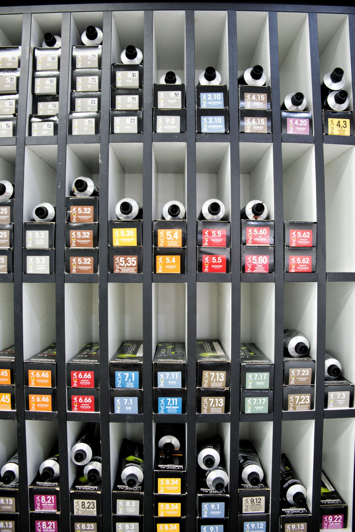 Wall shelving filled with professional hair color tubes organized by shade number at a hair salon.