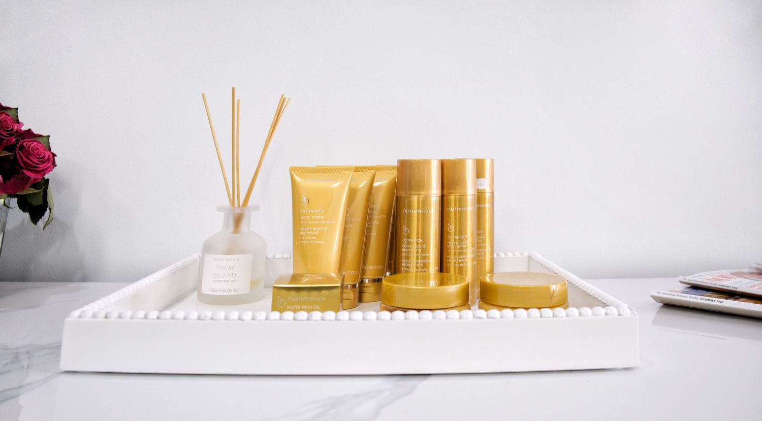 Gold hair care product tubes and a reed diffuser arranged on a white tray on a marble countertop.