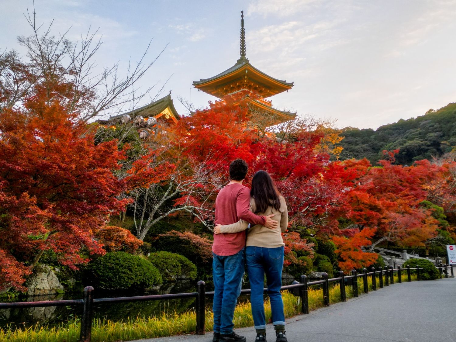 Couple embracing on a path while viewing a pagoda surrounded by vivid red autumn maple leaves in Kyoto.