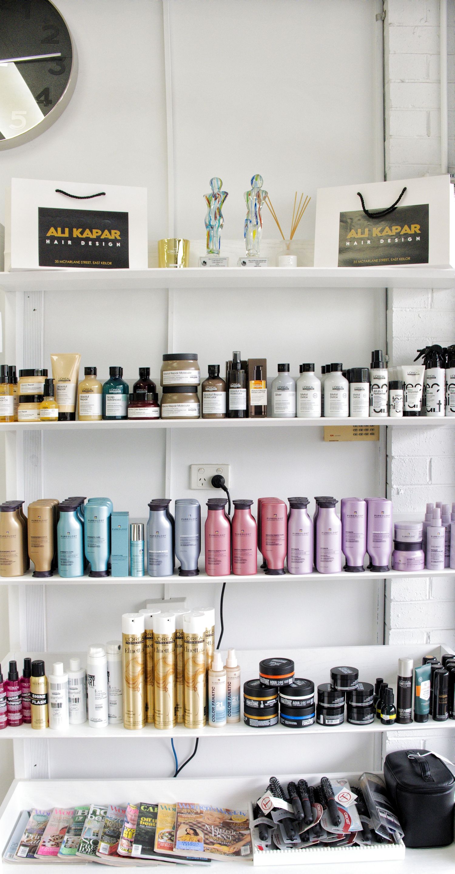 Salon retail shelves stocked with hair care products, Ali Kapar Hair Design bags, decorative figurines and styling tools.