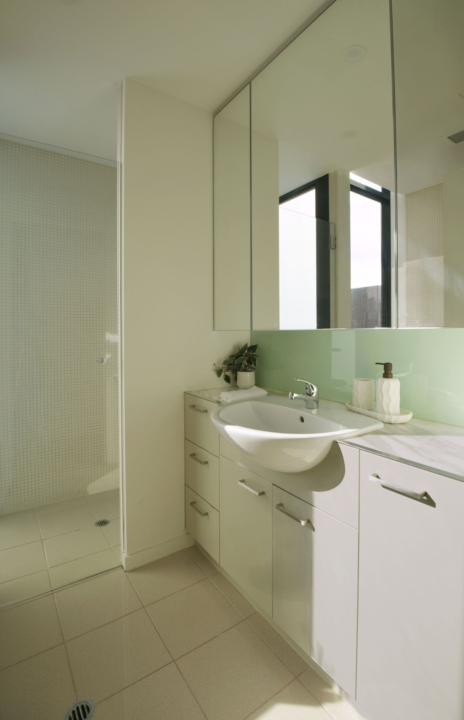 Modern white bathroom vanity with a round basin, mirrored cabinet, green splashback and glass shower enclosure.