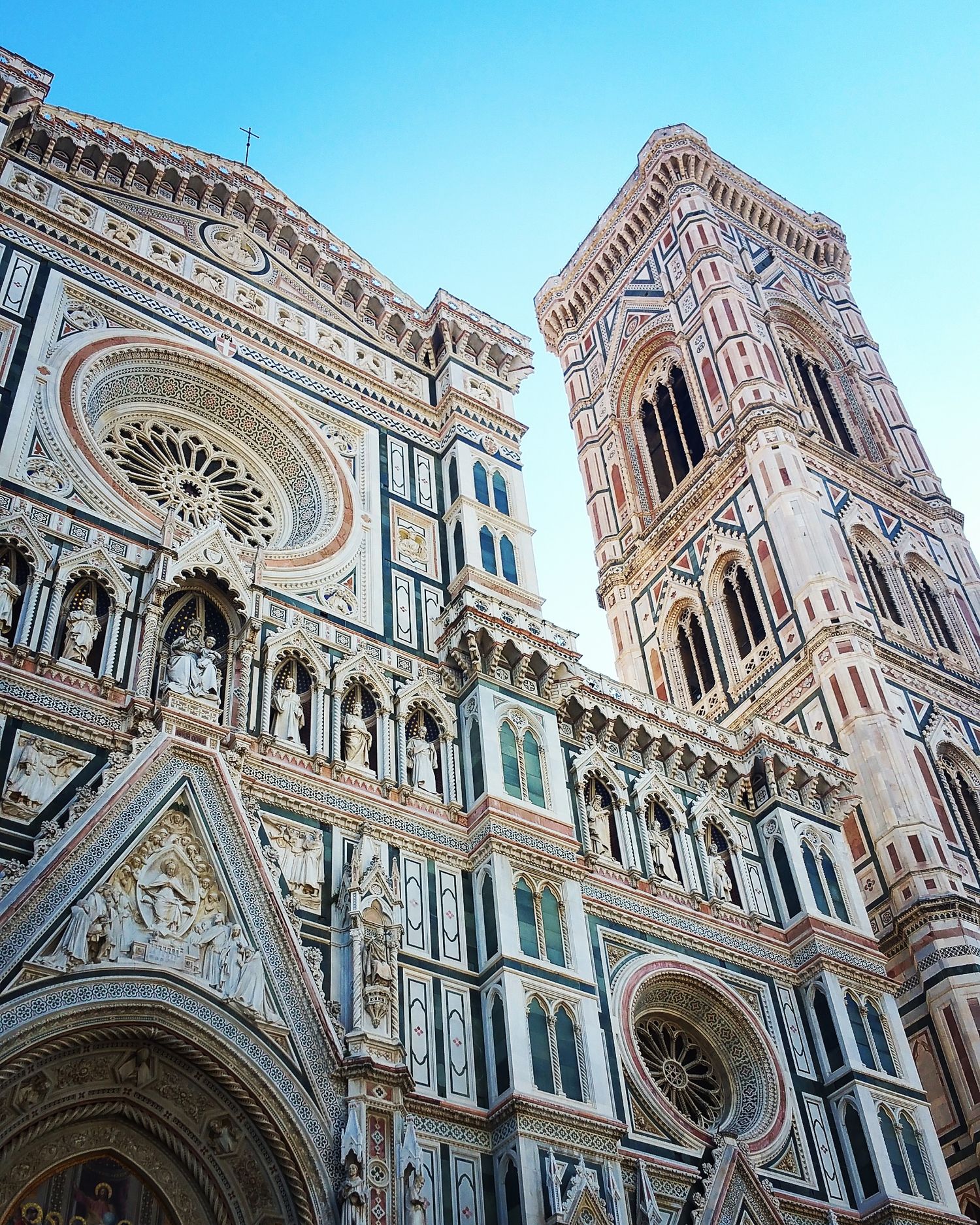 Ornate Florence Cathedral facade and Giotto's bell tower in pink, white and green marble against a blue sky.