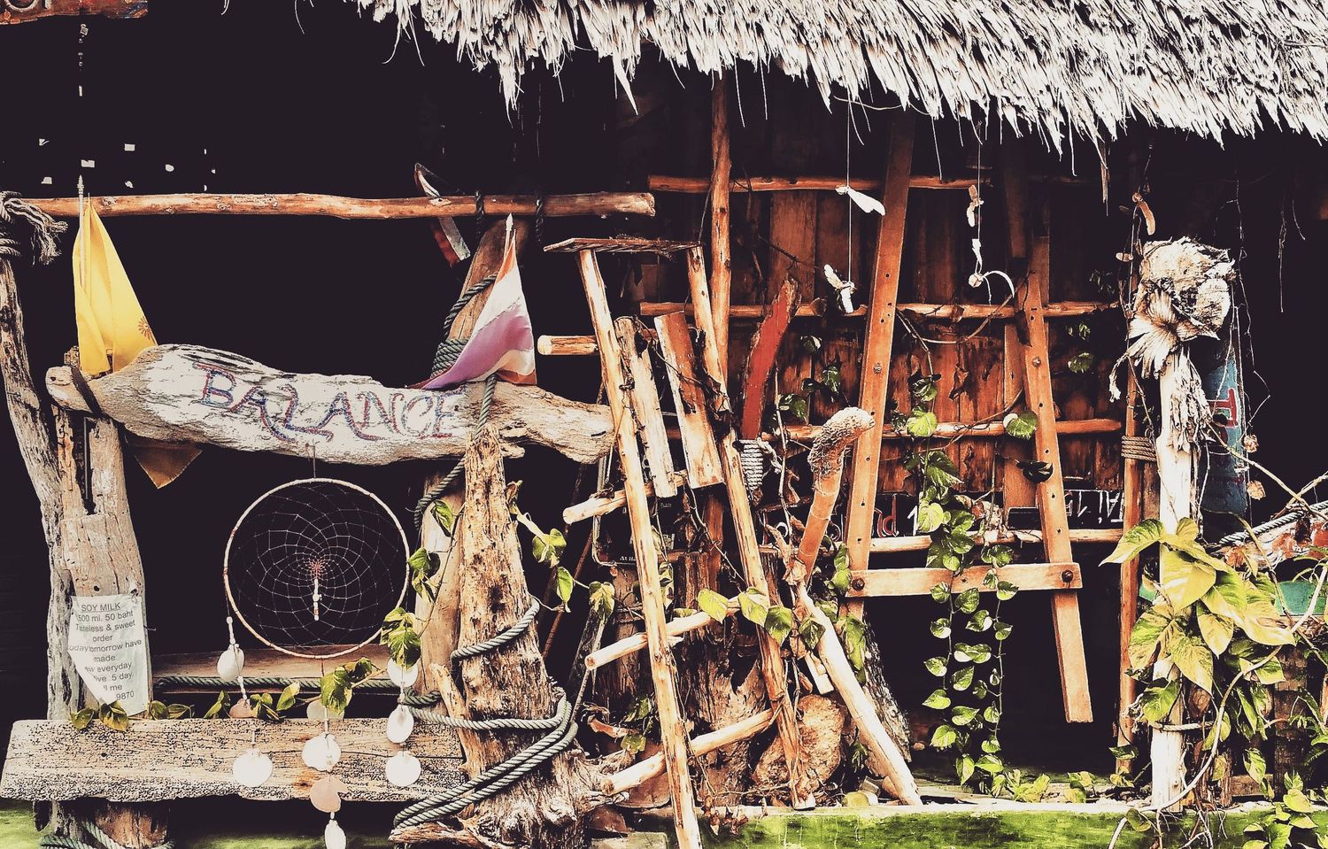 Rustic thatched-roof bamboo hut with a hand-painted Balance sign, hanging wind chimes and climbing green vines.