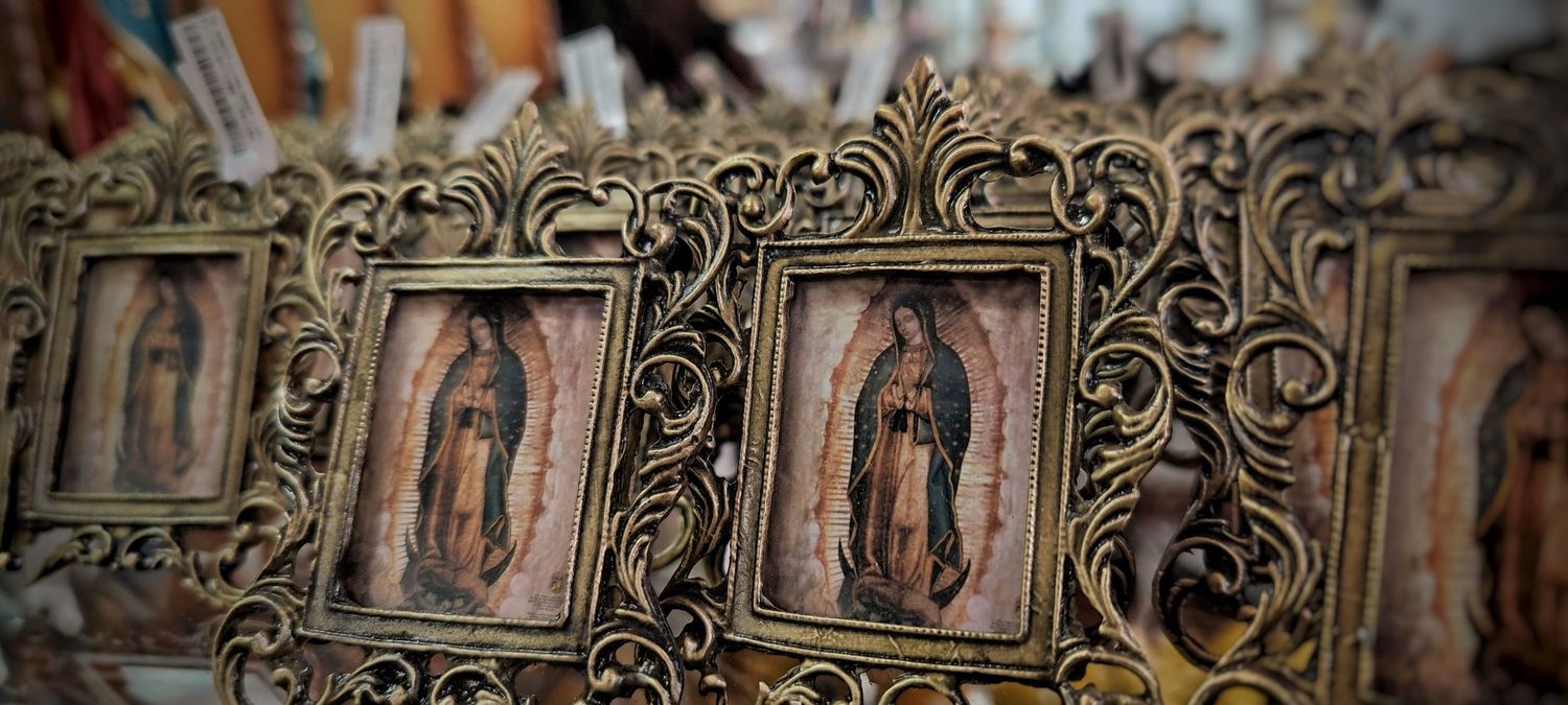 Row of ornate gold-toned picture frames holding images of the Virgin of Guadalupe, displayed at a Mexican market.