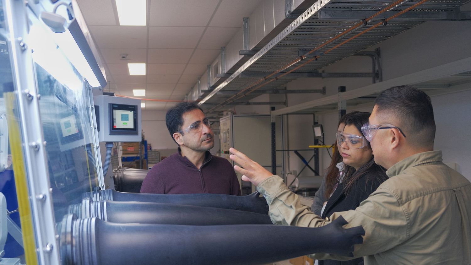 Three researchers examine equipment beside a glovebox in a battery research laboratory.