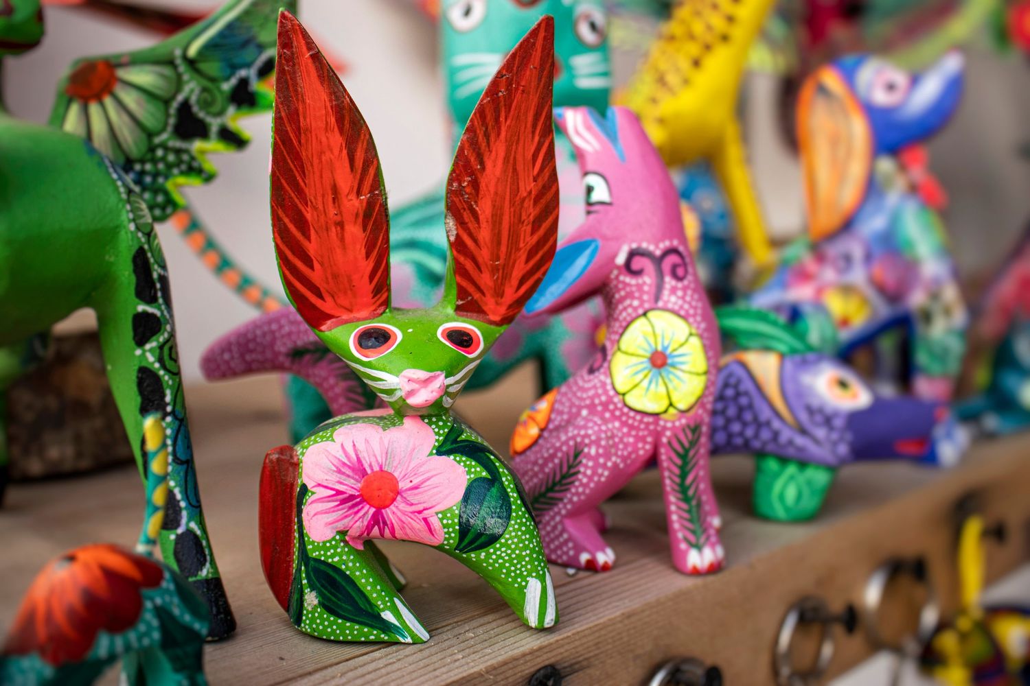 Colorful hand-painted wooden alebrije figures, including a green rabbit with red ears, displayed on a shelf.
