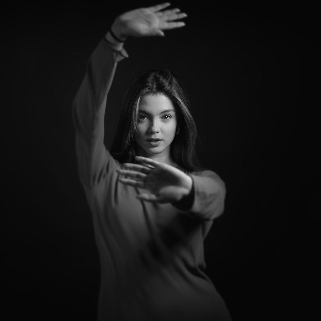 Black and white studio portrait of a young woman posing dynamically with arms extended forward.