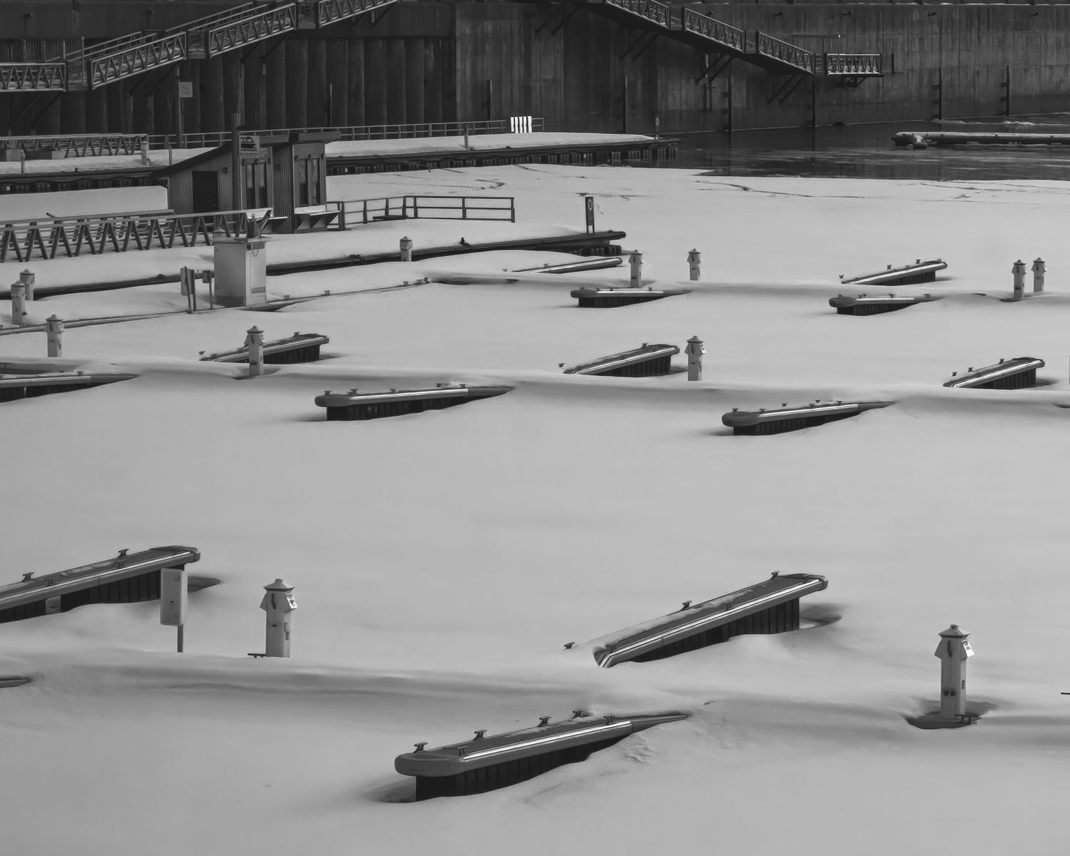 Black and white aerial view of a frozen marina with docks encased in snow and ice.