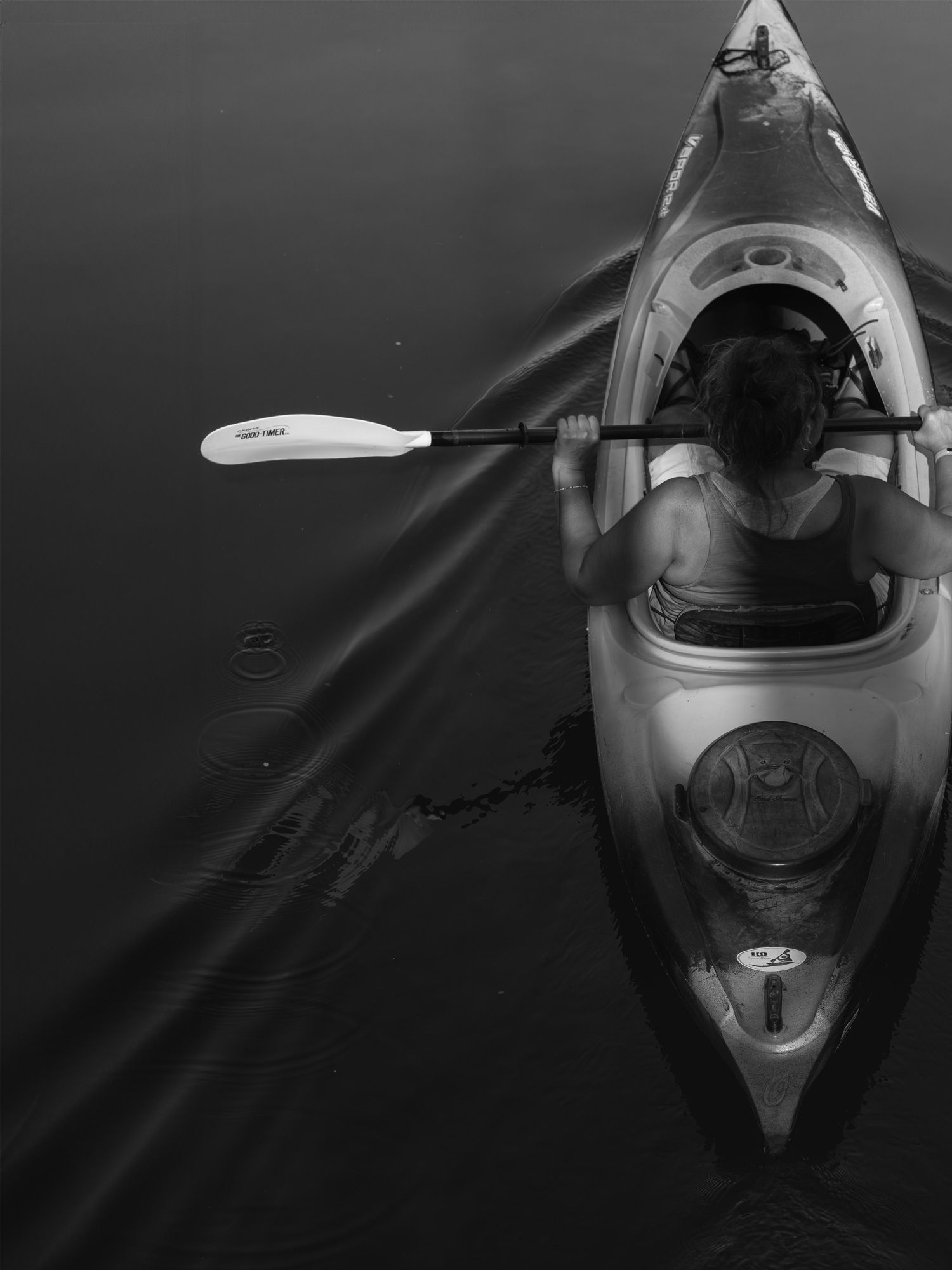 Aerial black and white view of a person kayaking on calm dark water with a paddle in hand.