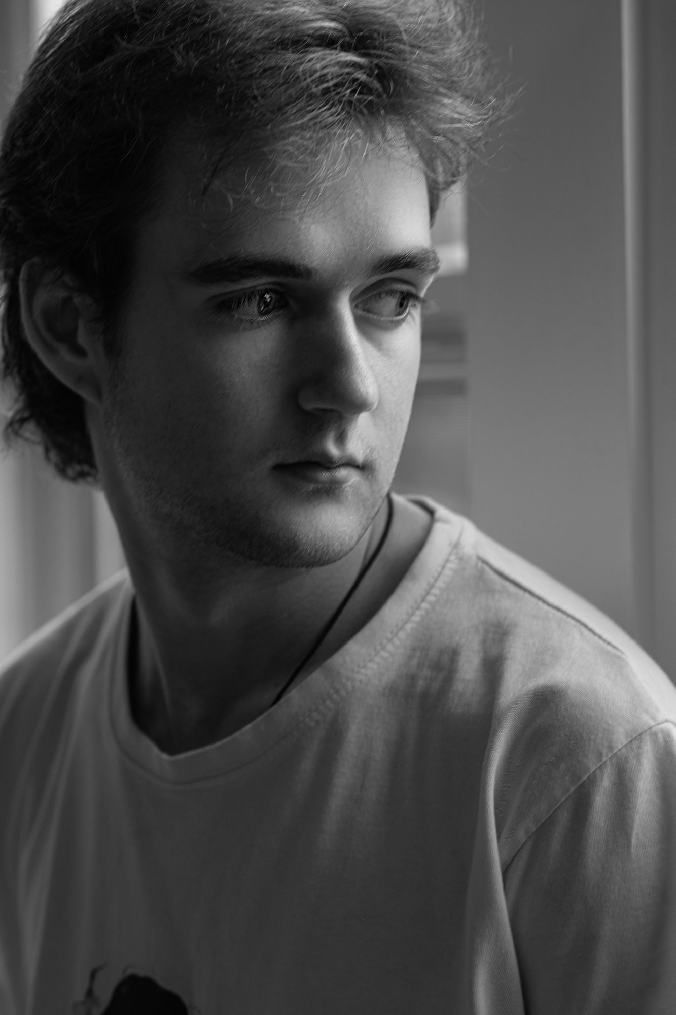 Black and white portrait of a young man in a white t-shirt looking away thoughtfully.
