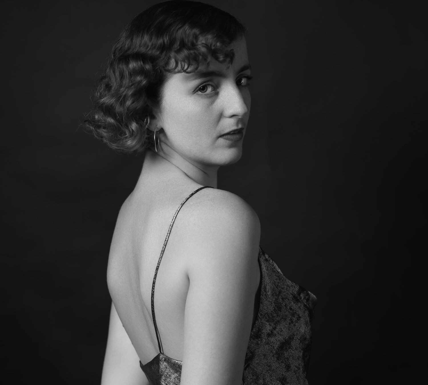 Black and white portrait of a curly-haired woman in a backless dress looking over her shoulder.