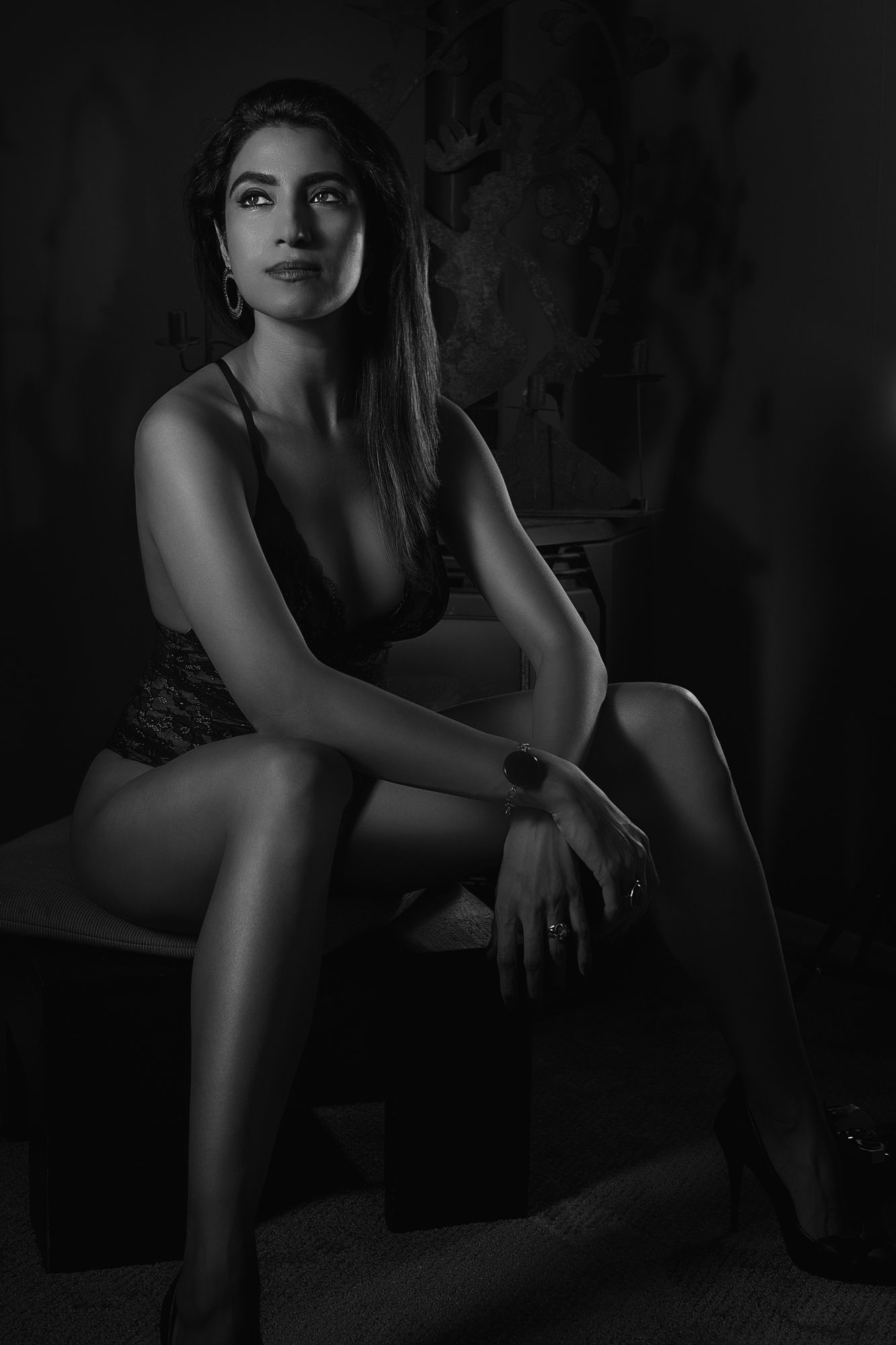 Black and white portrait of a woman in lingerie seated on a chair in dramatic studio lighting.