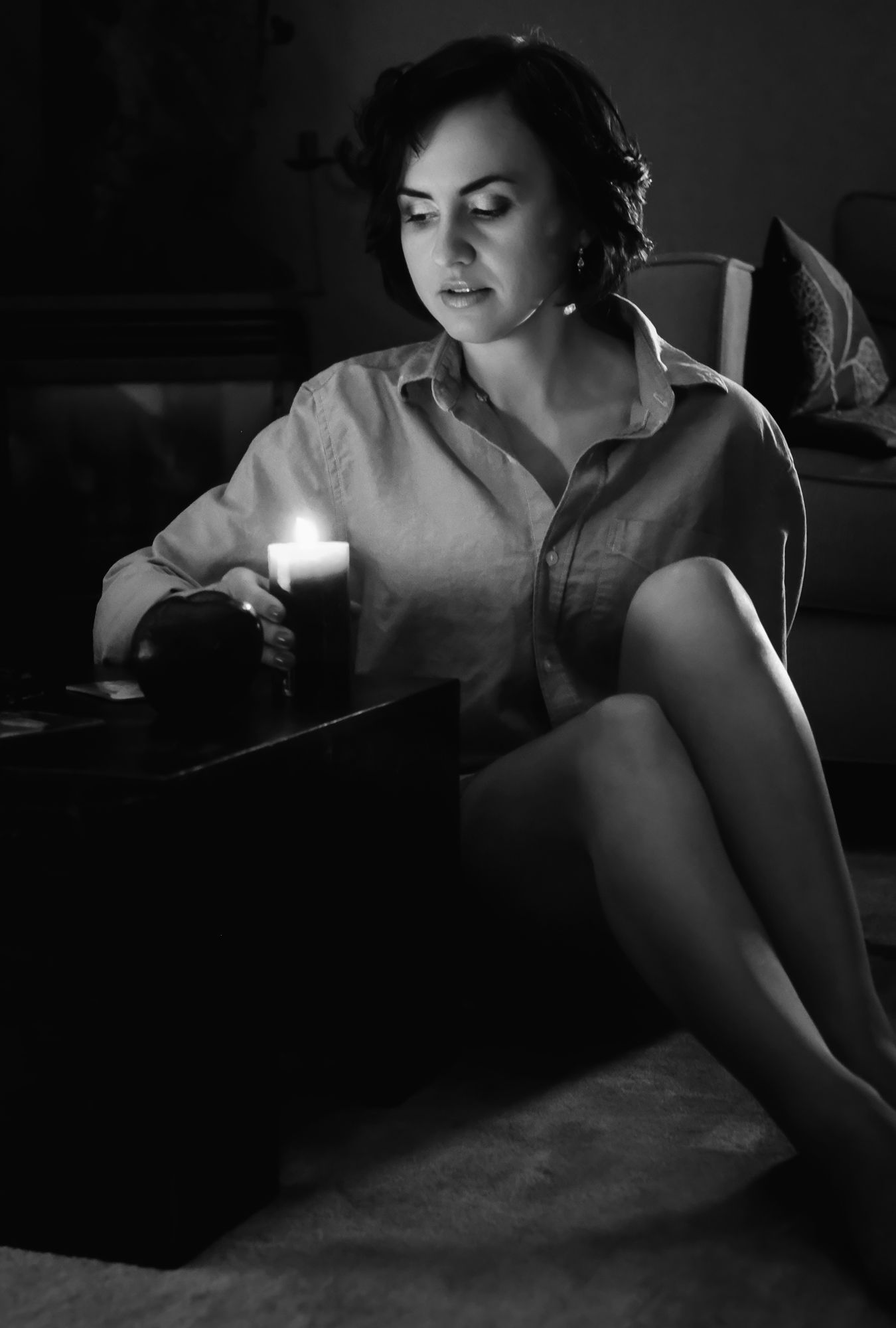 Black and white photo of a woman sitting on the floor by candlelight, working on a keyboard in a dimly lit room.