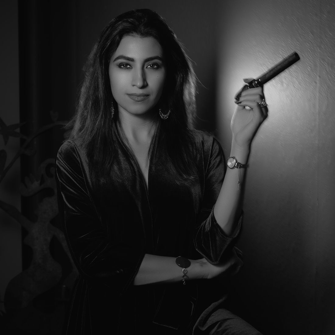 Black and white portrait of a woman holding a cigar in a velvet outfit with a watch.