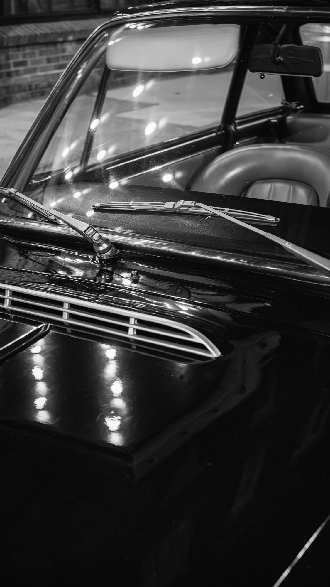 Close-up black and white photo of a shiny vintage classic car hood and windshield wipers.