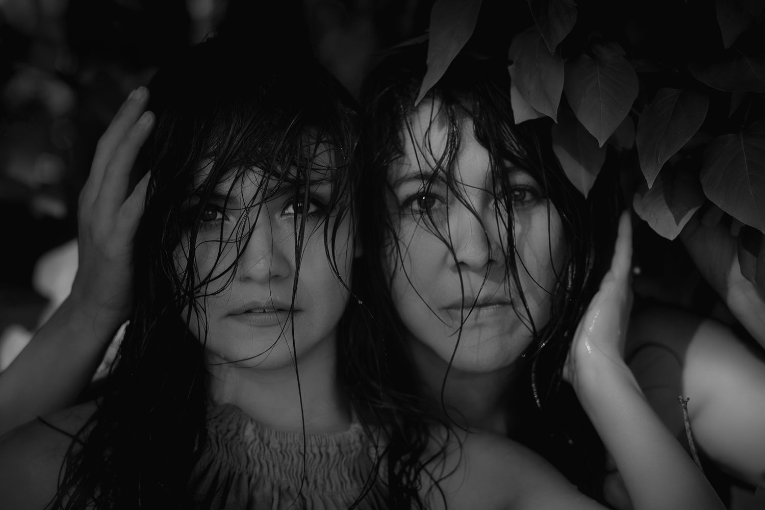 Moody black and white portrait of two women with wet hair surrounded by large leaves.