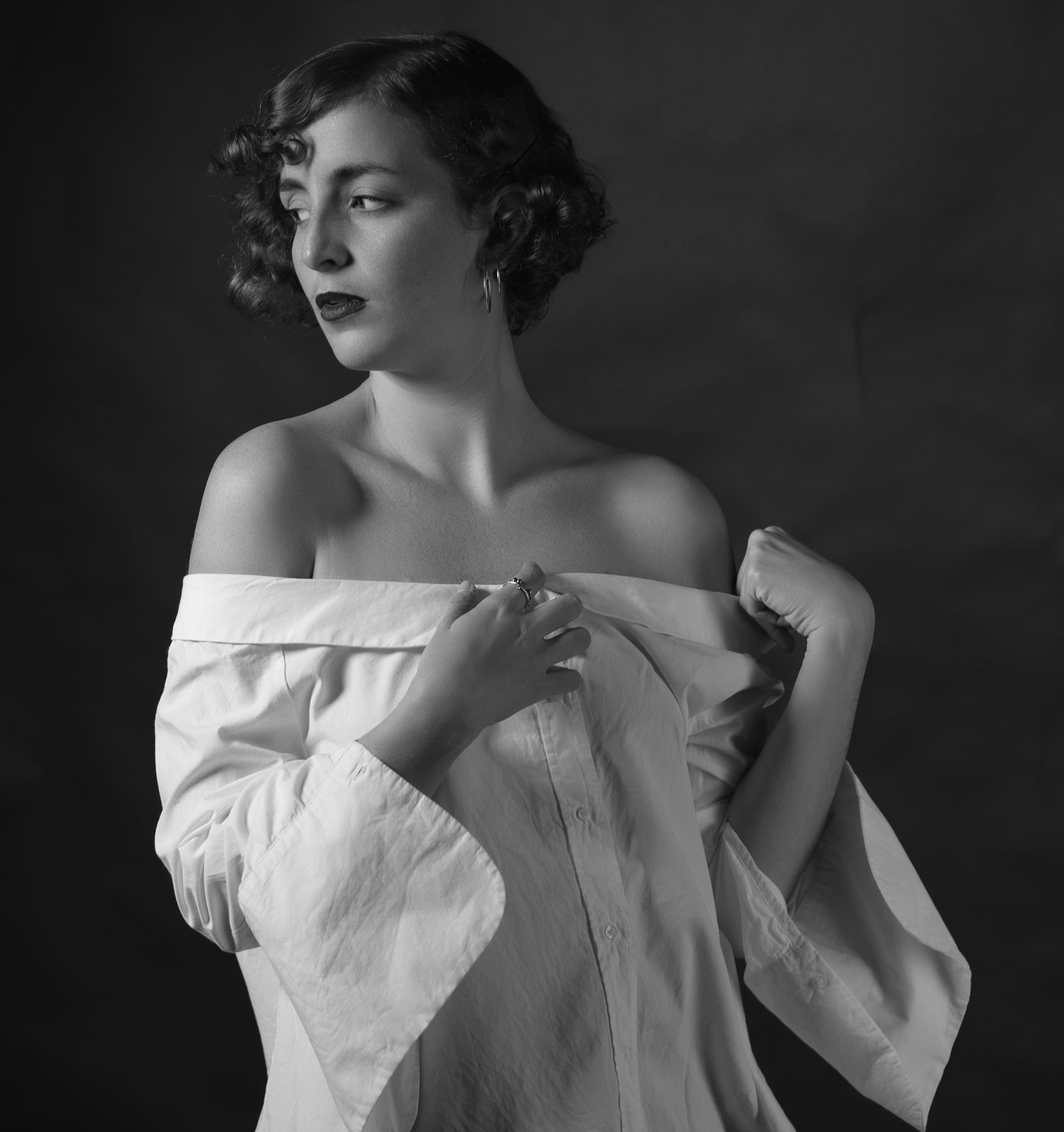 Black and white vintage-style portrait of a woman in an off-shoulder white shirt with curly hair.