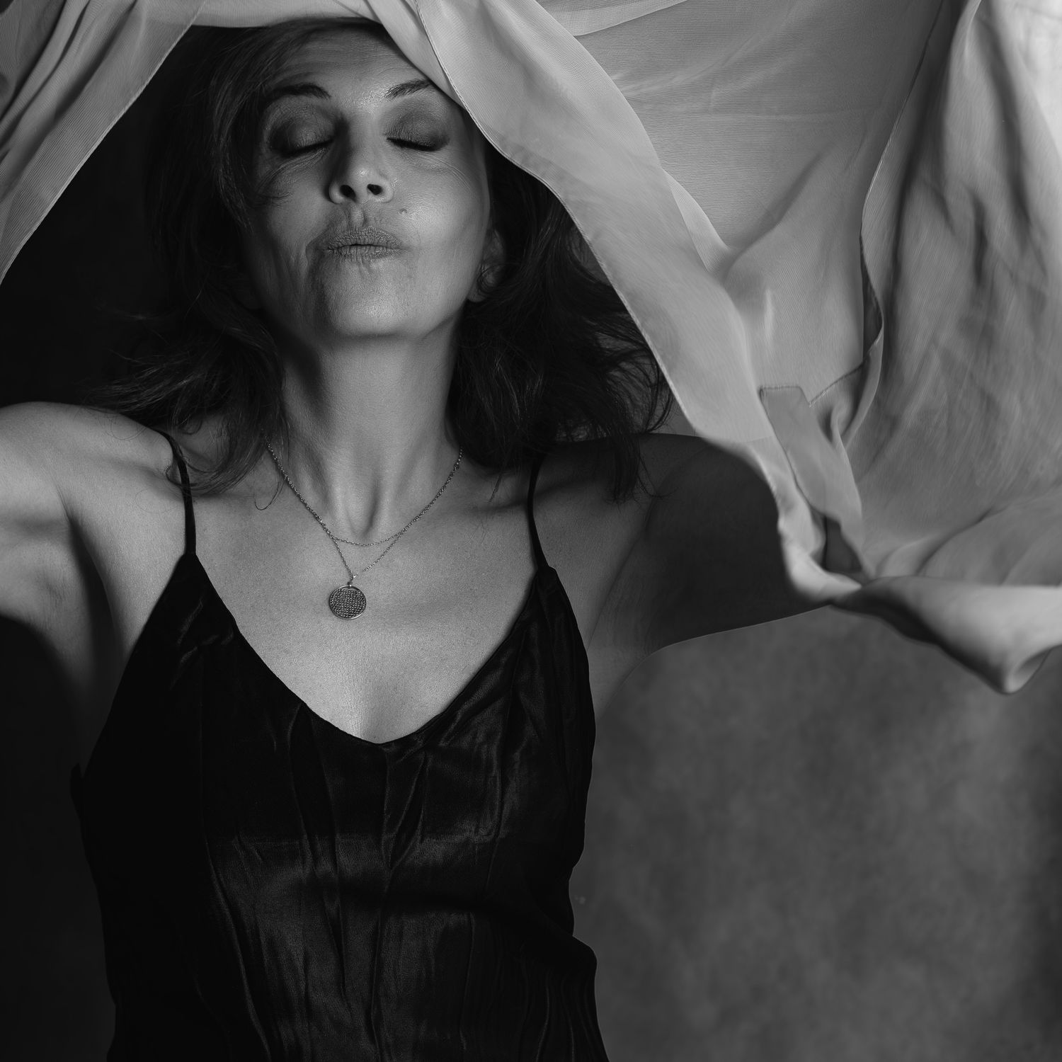 Black and white artistic portrait of a woman in silk camisole with flowing fabric overhead.