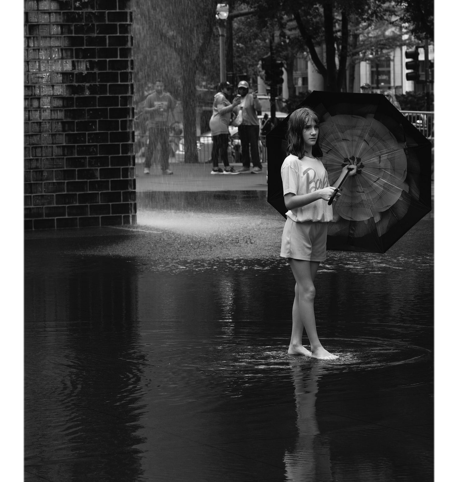Black and white photo of a young woman standing in a wet street holding an umbrella in the rain.