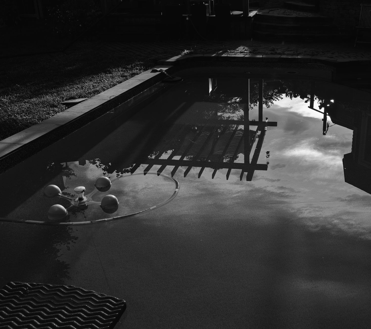 Aerial black and white view of a dark swimming pool with floating balls and reflections.