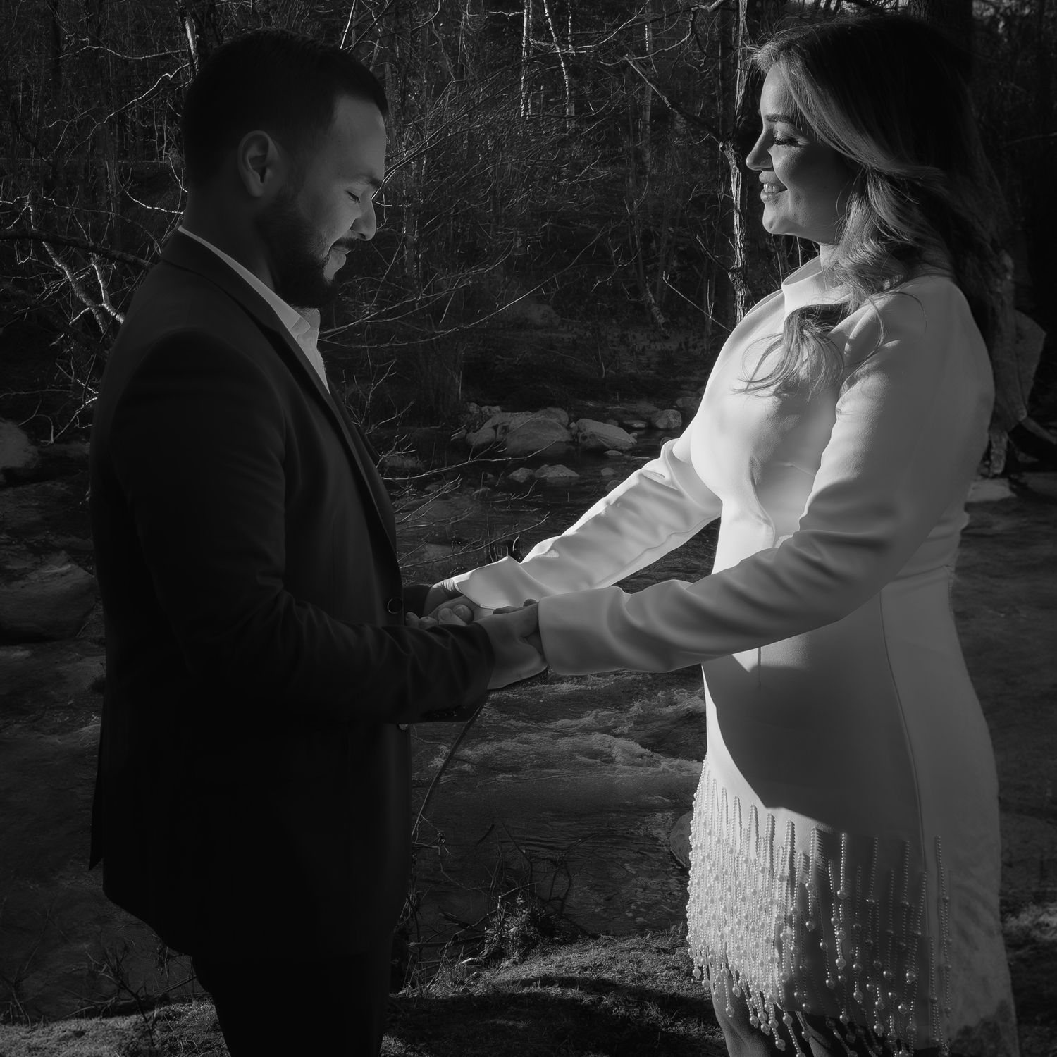 Black and white photo of a couple holding hands outdoors near a stream.