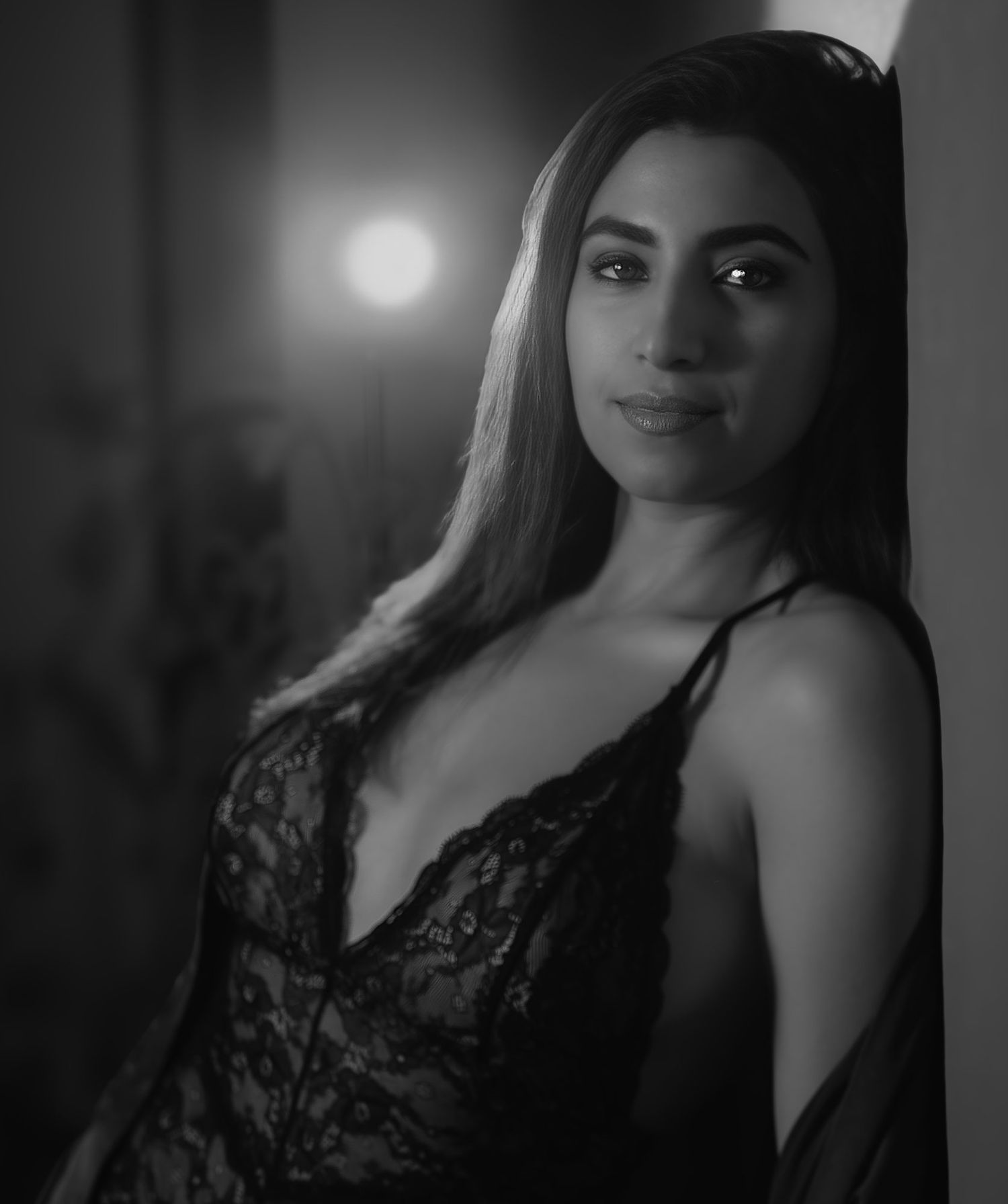 Black and white portrait of a woman in black lace camisole smiling softly in dramatic lighting.
