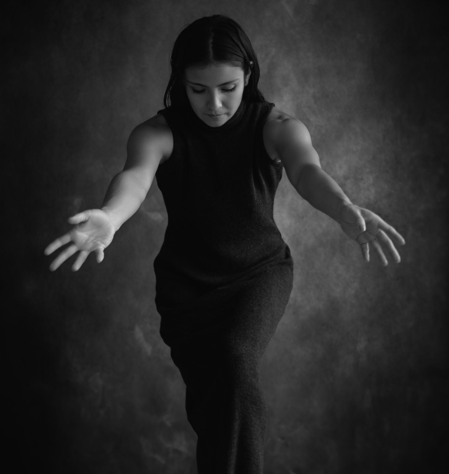 Black and white photo of a woman in a sleeveless dress, arms outstretched, striking a dramatic dance pose.