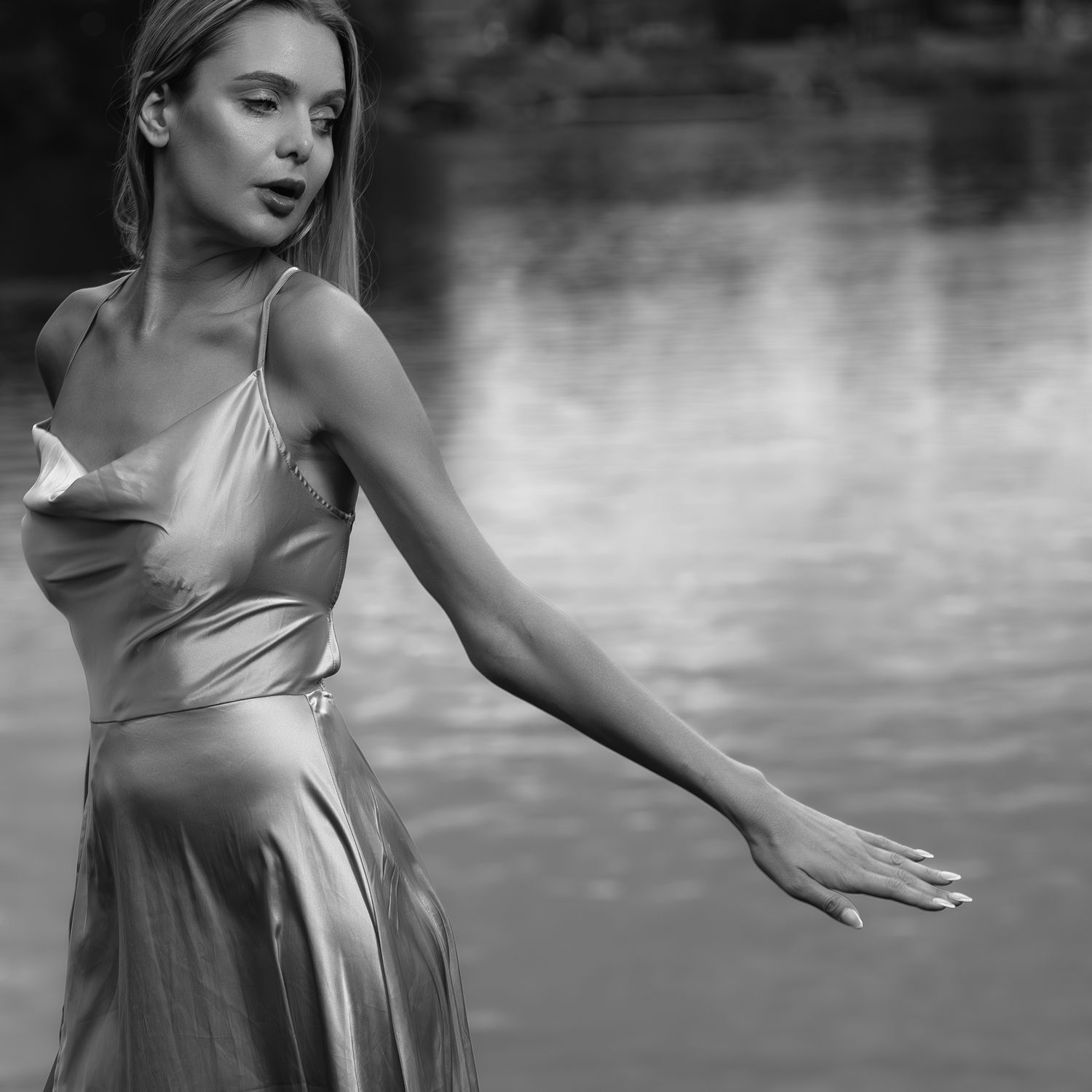 Black and white portrait of a blonde woman in a satin slip dress posing near a reflective lake.