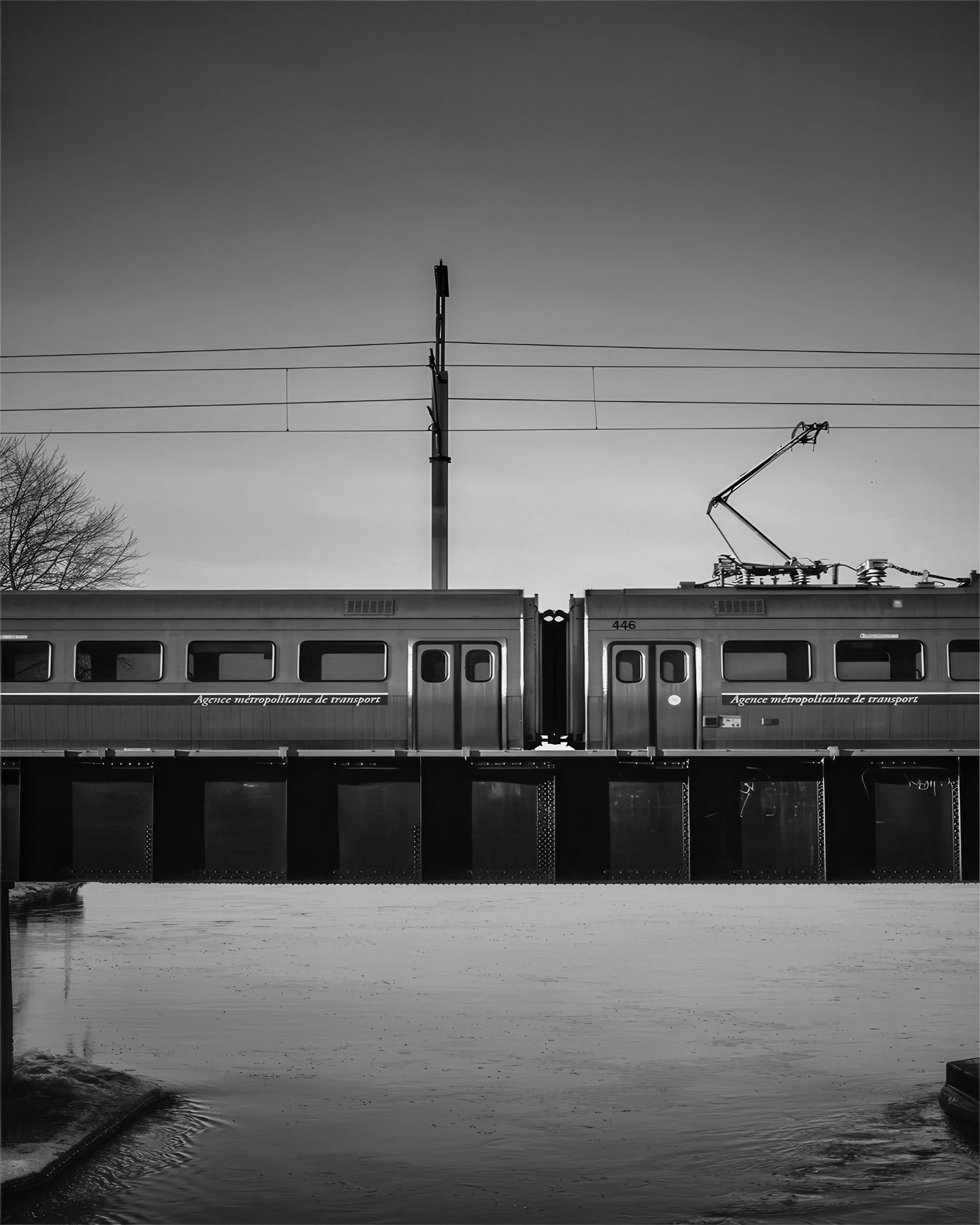 Black and white photo of two subway trains on an elevated track over a waterway.