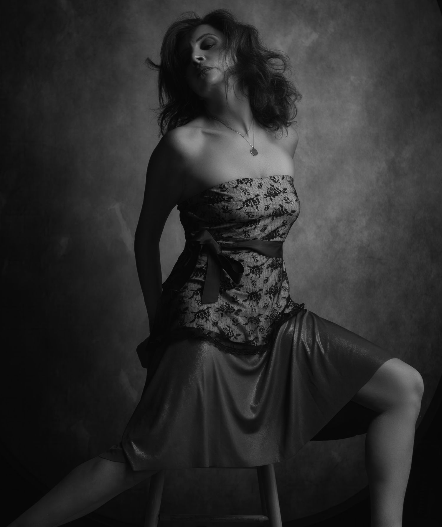 Black and white dramatic studio portrait of a woman in strapless floral dress seated on a stool.