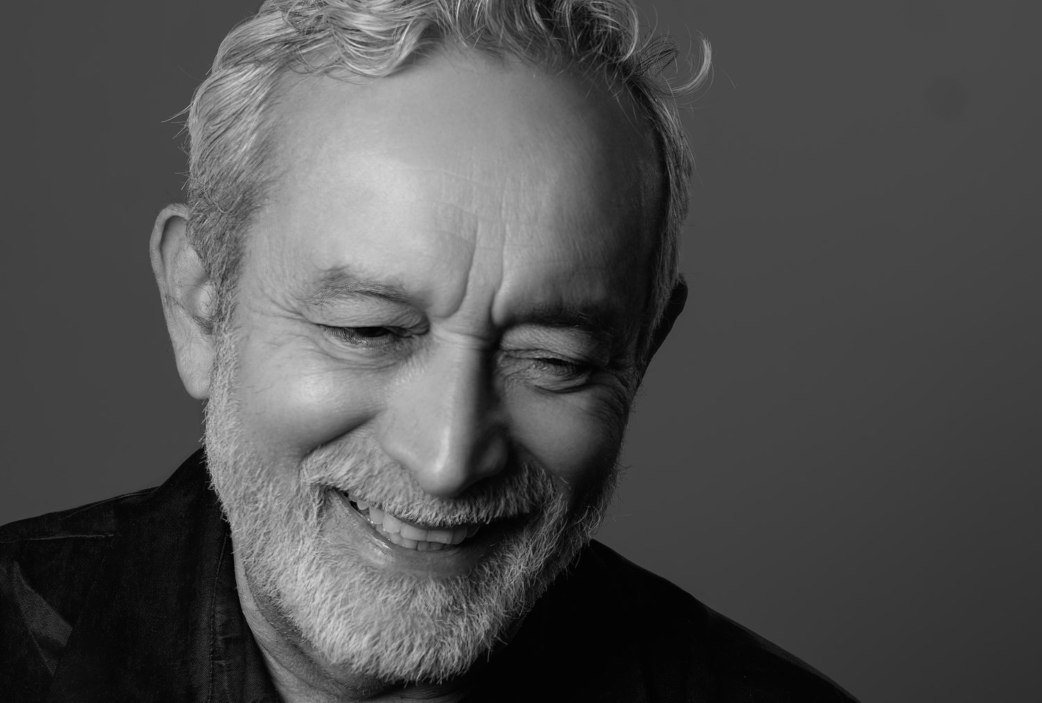 Monochrome portrait of a happy older man with gray stubble beard laughing with eyes closed.