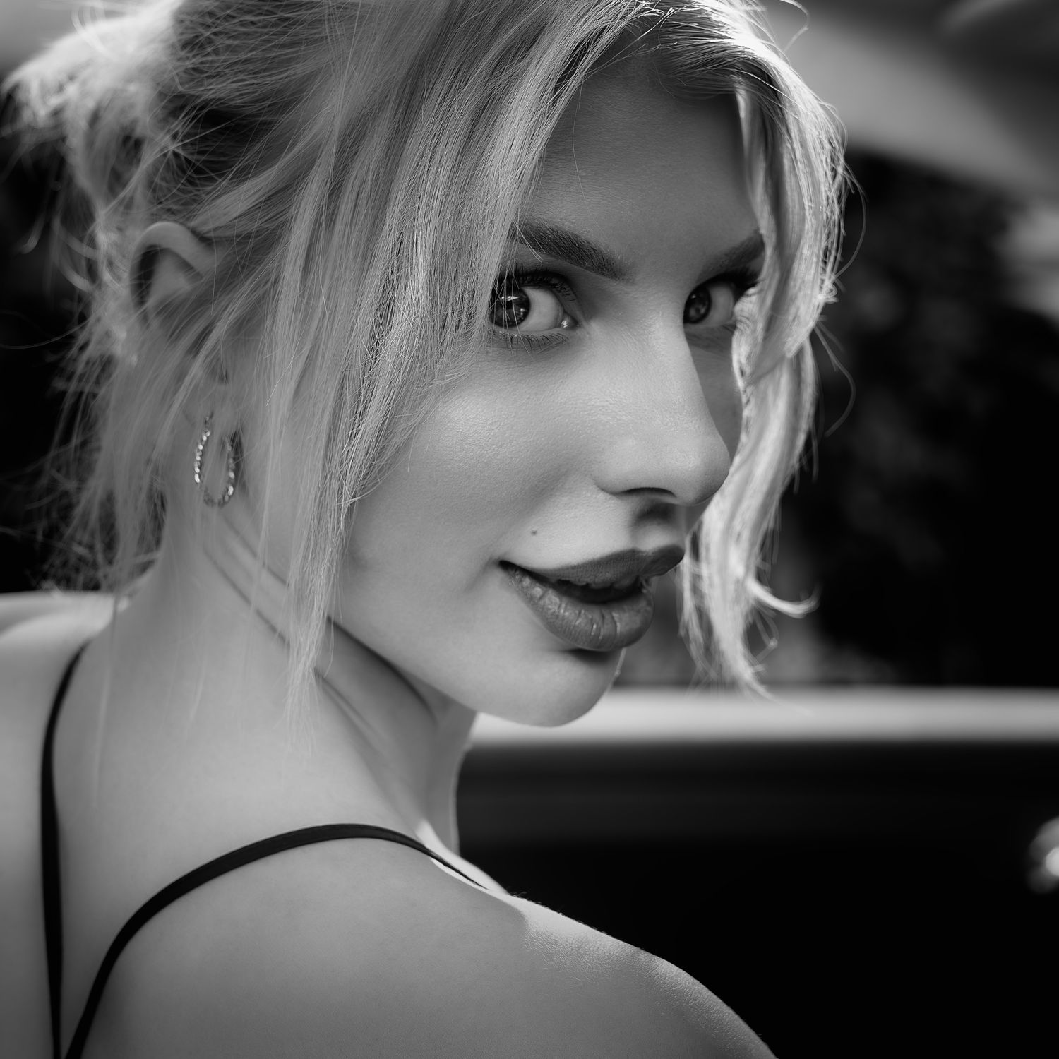 Black and white close-up portrait of a blonde woman with hoop earrings glancing over her shoulder.