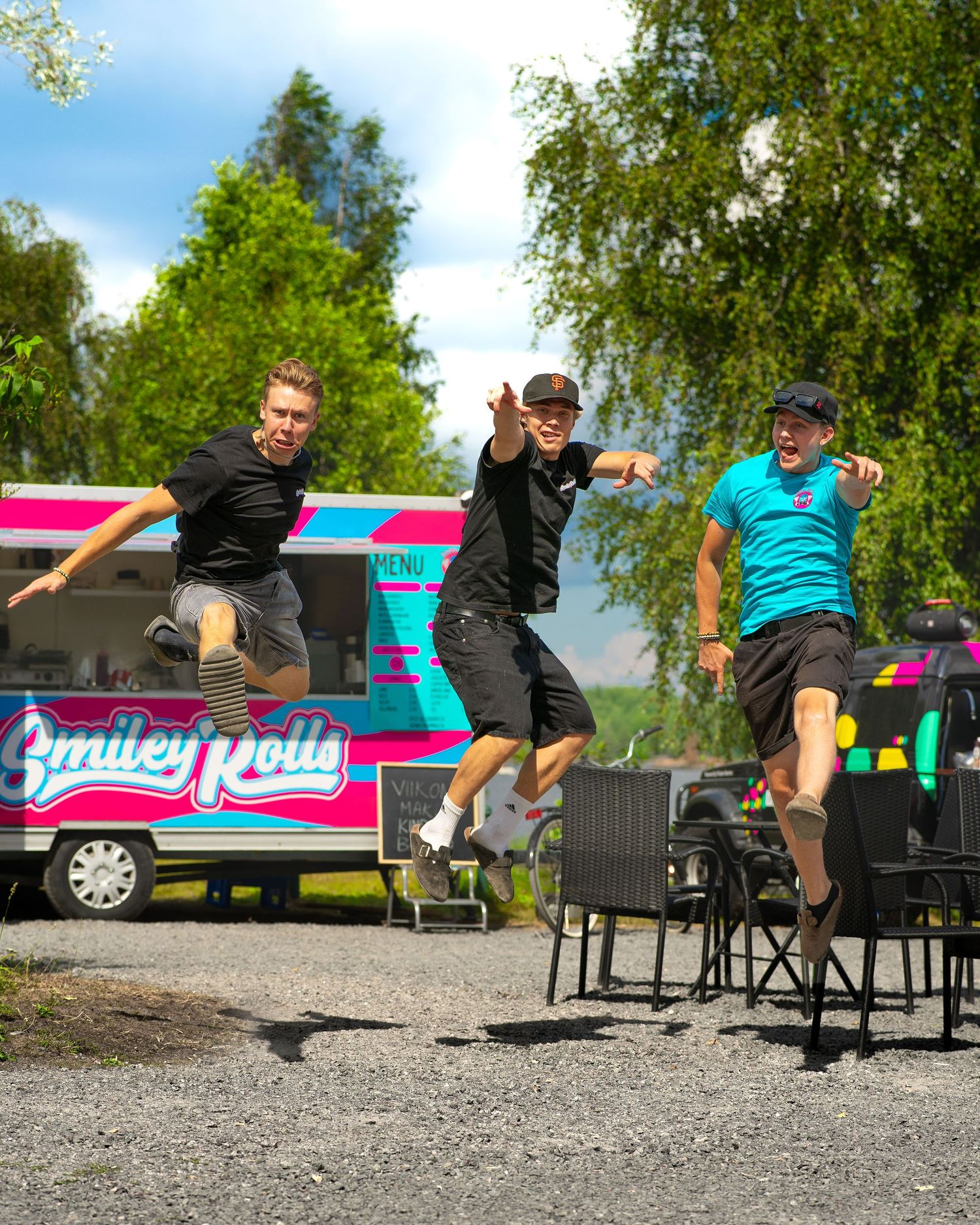 Three men jumping joyfully in front of a colorful Smiley Rolls food truck on a sunny day brand photoshoot.