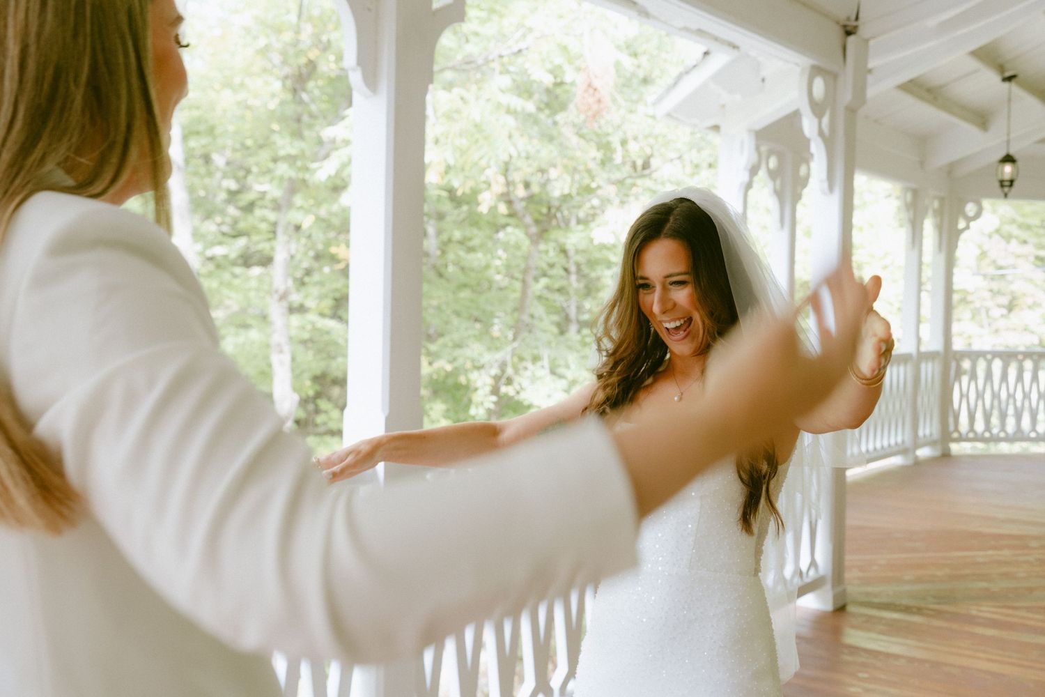 Joyful bride in white dress and veil laughs during first look on porch.