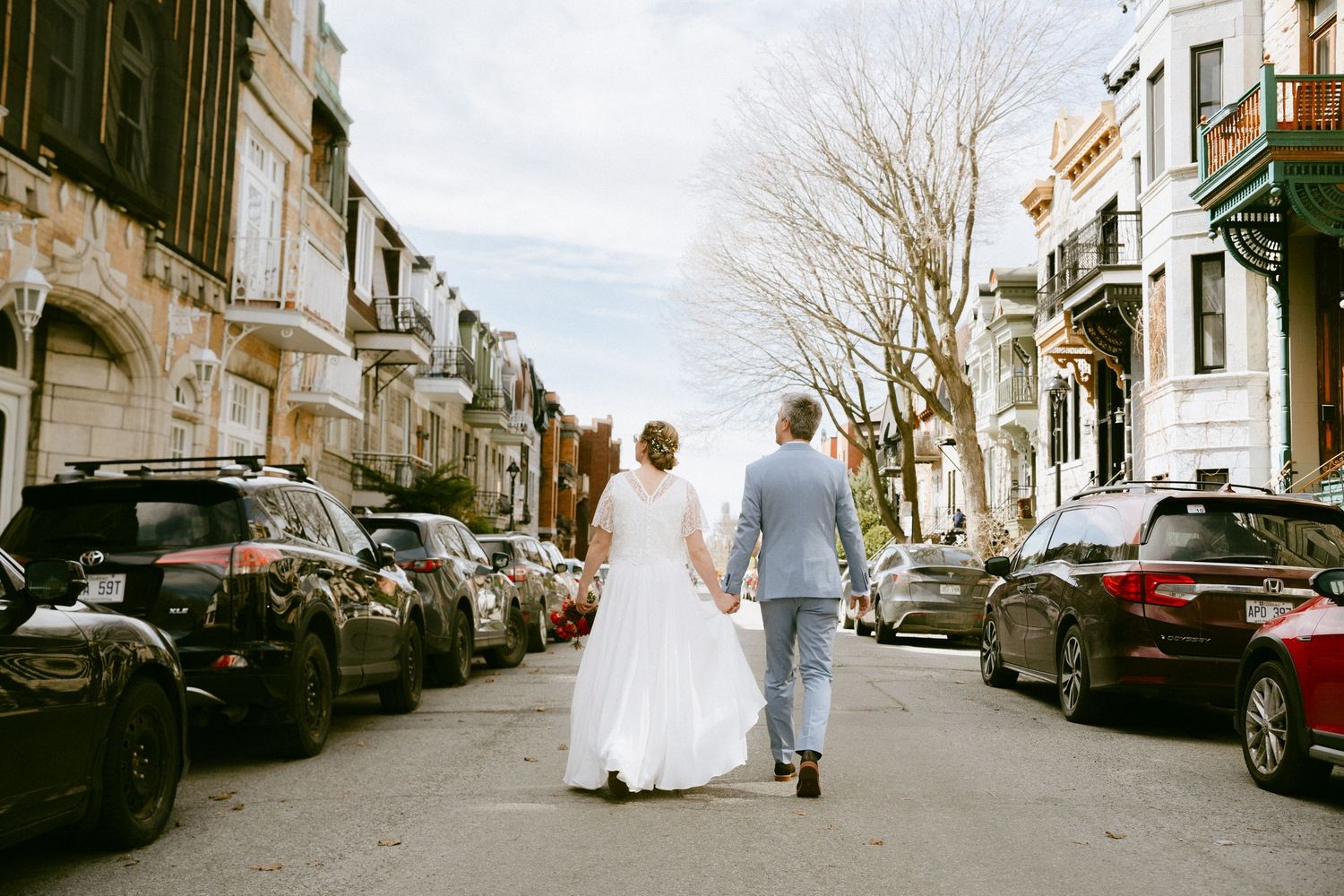 Bride and groom walk hand in hand down the middle of a charming city street.