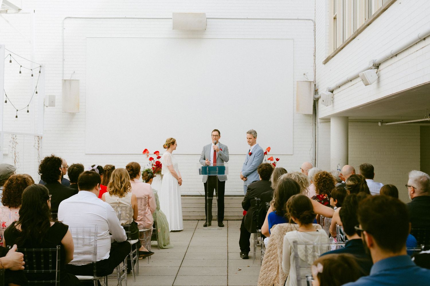 Wedding ceremony in modern white venue with bride, groom, and officiant at altar before seated guests.