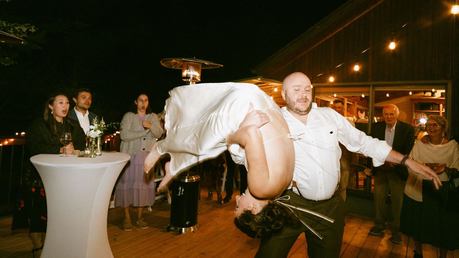Groom spinning bride upside down in dramatic dance move at outdoor wedding reception.