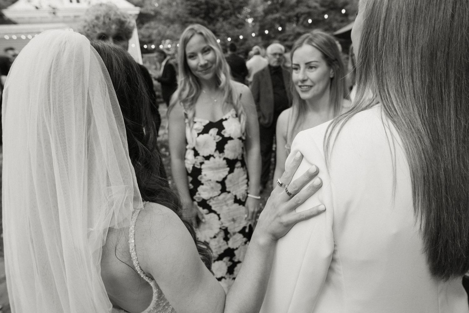 Bride in wedding veil chatting with guests in floral dress at outdoor wedding reception.