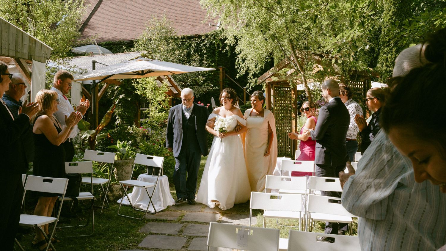 Bride walks down garden aisle with escort during outdoor wedding ceremony.