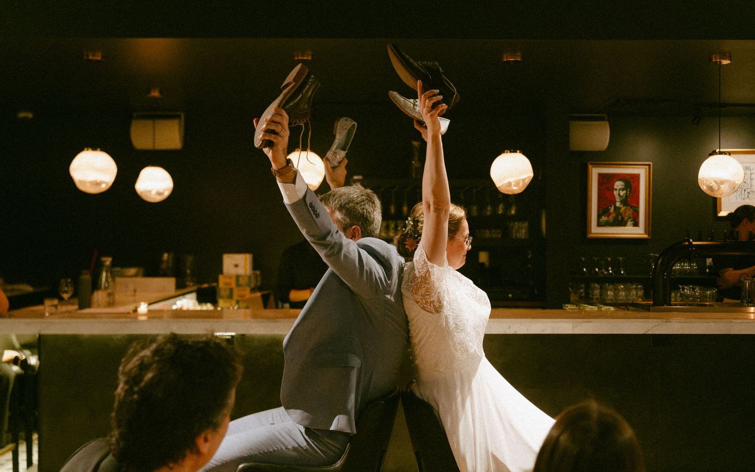 Bride and groom raising shoes in the air at wedding reception bar celebration.